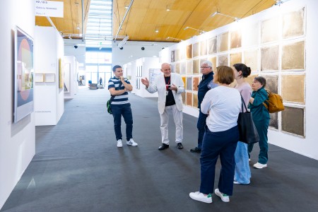 Besucher schauen sich ein Gemälde an. Ein Galerist erklärt Ihnen das Bild.