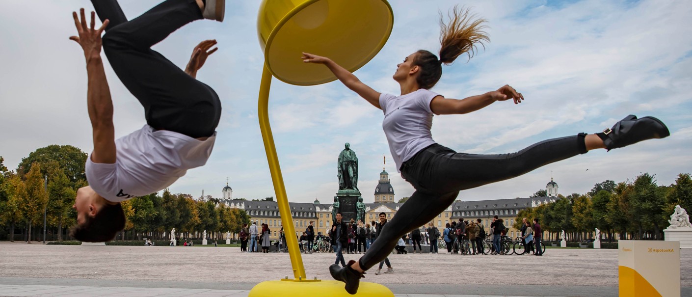 Dancers dance in front of a lamp. Karlsruhe Castle in the background.